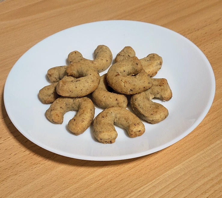 Vánoční vanilkové rohlíčky s lískovymi ořísky a kokosovým cukrem na bílém talíři a dřevěném podkladu z bezobalových surovin.